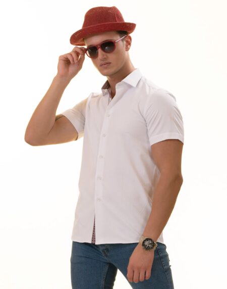 A man wearing a white paisley short sleeve shirt with a spread collar, paired with a red hat and sunglasses, standing against a white background.