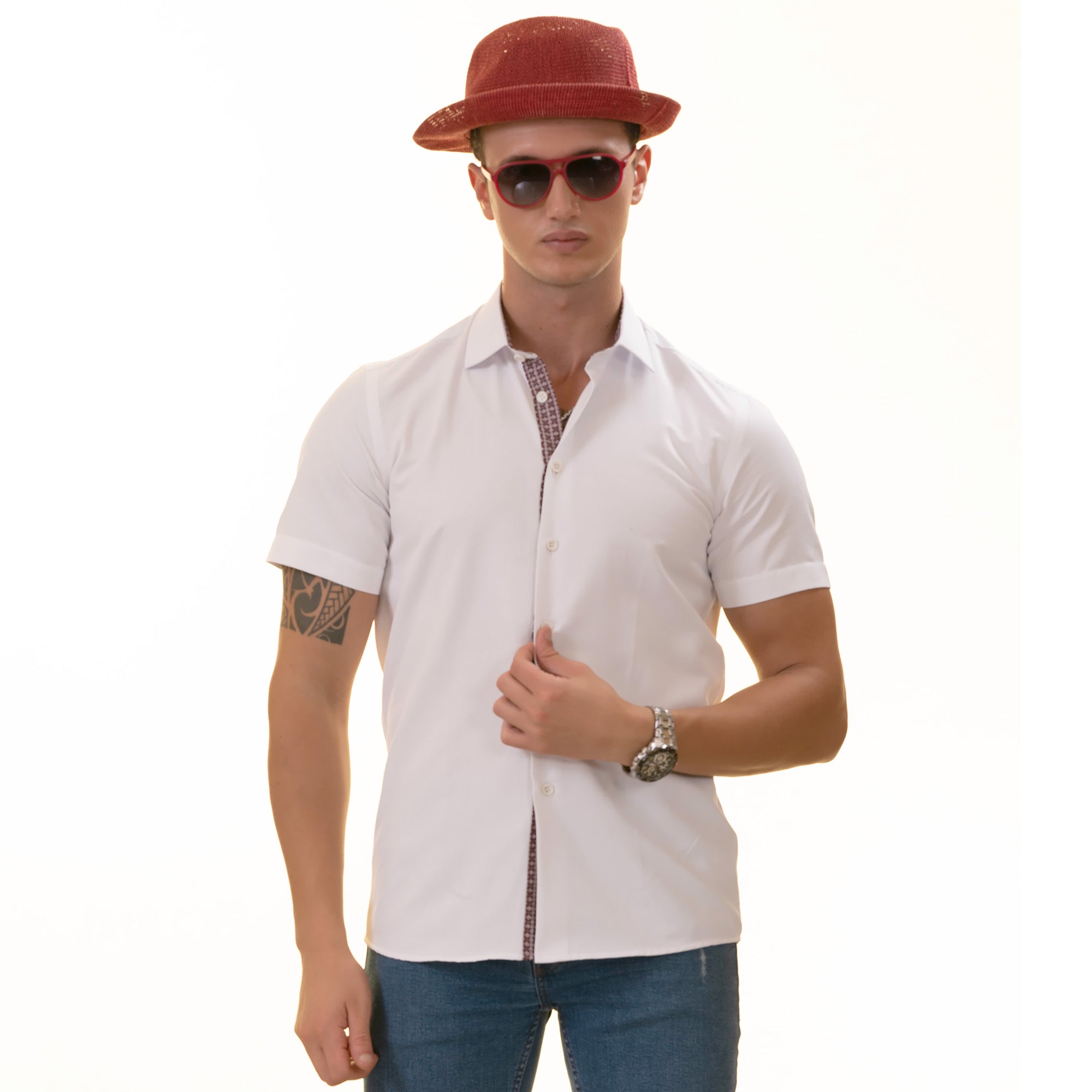 A man wearing a white paisley short sleeve shirt with a spread collar, paired with a red hat and sunglasses, standing against a white background.