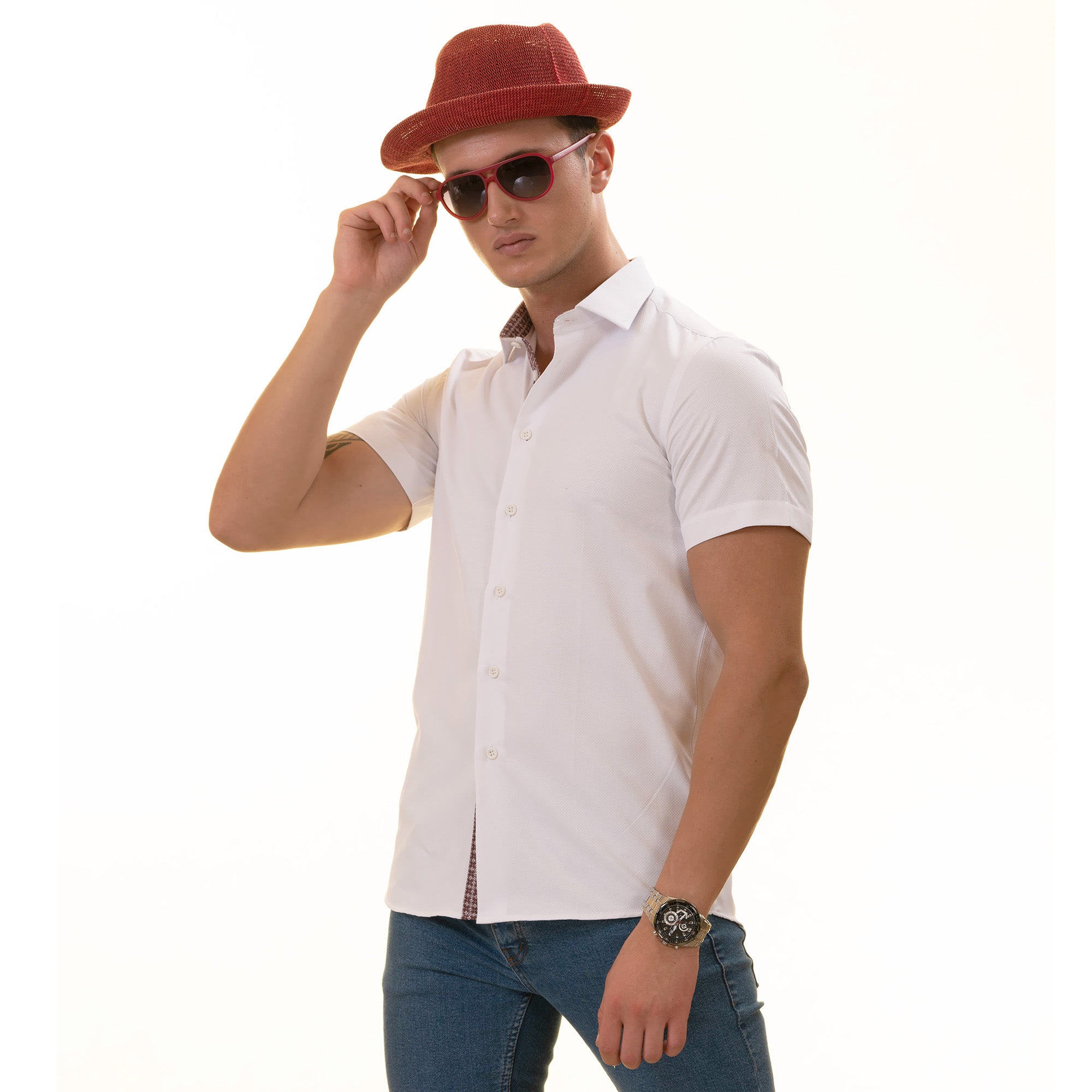 A man wearing a white paisley short sleeve shirt with a spread collar, paired with a red hat and sunglasses, standing against a white background.